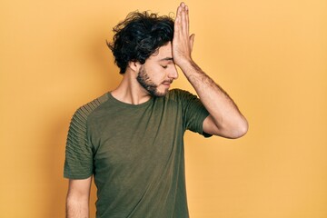 Handsome hispanic man wearing casual green t shirt surprised with hand on head for mistake,...
