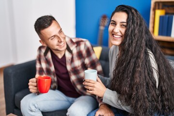 Man and woman couple drinking coffee sitting on sofa at home