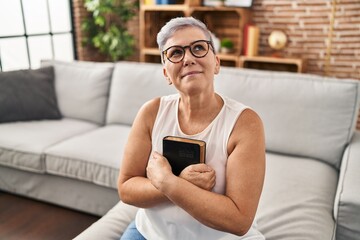 Middle age woman hugging bible sitting on sofa at home