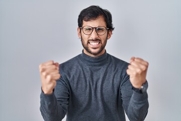 Handsome latin man standing over isolated background angry and mad raising fists frustrated and furious while shouting with anger. rage and aggressive concept.