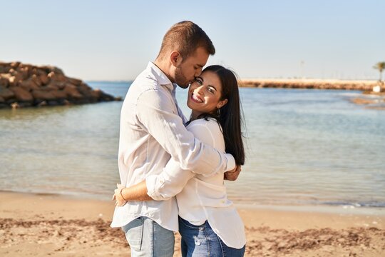 Man and woman couple smiling happy hugging each other standing at seaside
