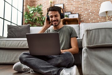Young hispanic man using laptop and headphones at home