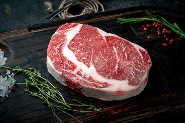 One Raw rib eye steak on a wooden Board on a table prepared for the grill with spices and herbs. Rustic style