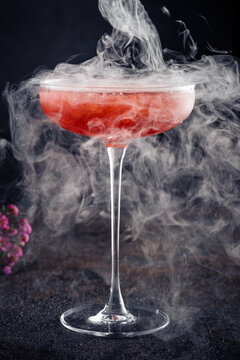 Strawberry margarita cocktail in a beautiful glass with crushed ice and smoke on a dark background. Tropical alcoholic drink with tequila, close up