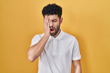 Arab man standing over yellow background yawning tired covering half face, eye and mouth with hand. face hurts in pain.