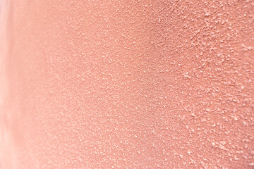 Close-up of a plastered and rough concrete or stone wall painted in peach color. Side view. High resolution full frame textured background. Copy space.