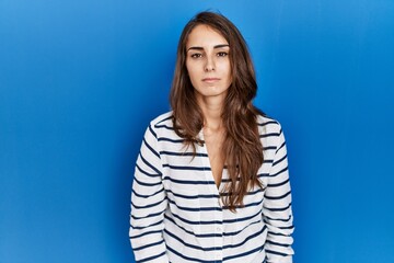 Fototapeta premium Young hispanic woman standing over blue isolated background relaxed with serious expression on face. simple and natural looking at the camera.