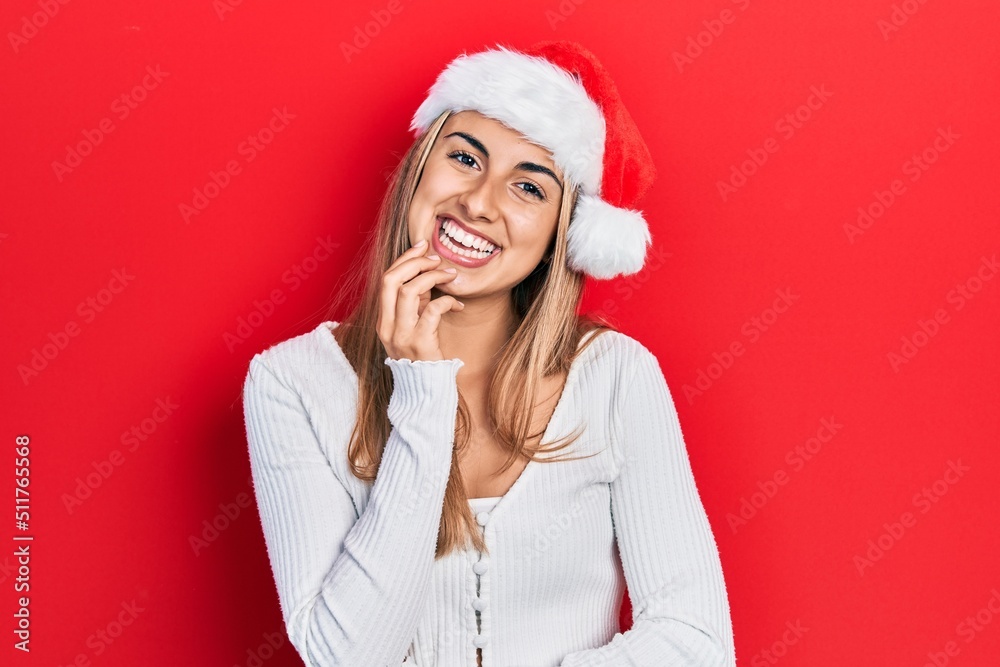 Poster beautiful hispanic woman wearing christmas hat looking confident at the camera with smile with cross