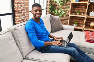 Young african american man using laptop sitting on sofa at home