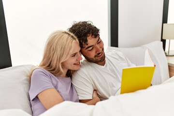 Young beautiful couple reading book lying in bed at home.