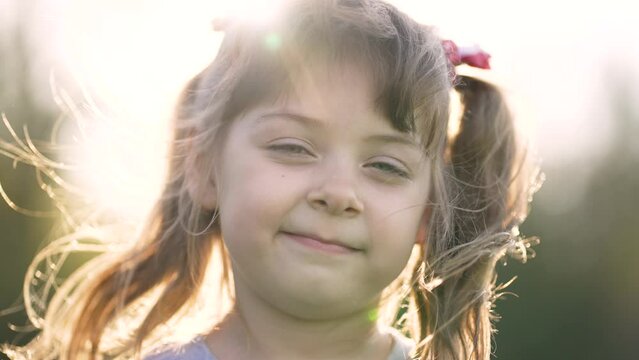 Happy girl in the sun in wind. Close-up of the girl face in the park. Dream girl. Hair in the wind. The child smiles at the camera. Girl's dream. Face close-up. Happy child in the park. Beautiful face