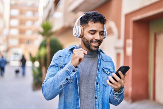 Young hispanic man smiling confident listening to music at street