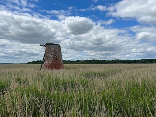 Ancient brick windmill building in nature reserve coastal landscape in Walberswick heath by the beach East Anglia in England uk with grassy reed banks, trees with blue white cloud sky on Summer day
