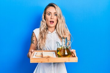 Beautiful young blonde woman holding tray with olive oil and bread toast afraid and shocked with surprise and amazed expression, fear and excited face.