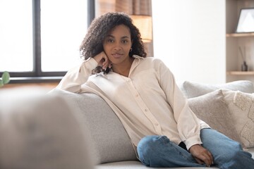 Portrait of lovely young mixed race woman smiling and looking at camera, sitting on sofa at home