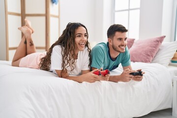 Young hispanic couple playing video game lying on bed at bedroom