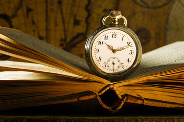 Antique pocket watch on opened old book. Old map on background