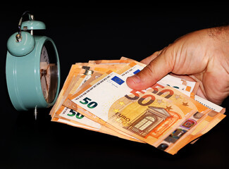 Concept of time and money. Hand of a man holding bills in front of a watch.