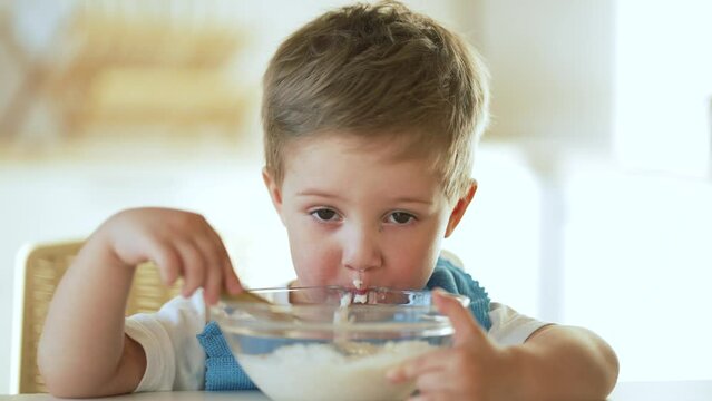 baby eats cereal porridge.Child sits at table and eats porridge.Family breakfast in kitchen.Child at table in kindergarten.Child proper nutrition.Breakfast in kindergarten.Happy dirty child with spoon