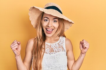 Young caucasian woman wearing summer hat celebrating surprised and amazed for success with arms raised and open eyes. winner concept.