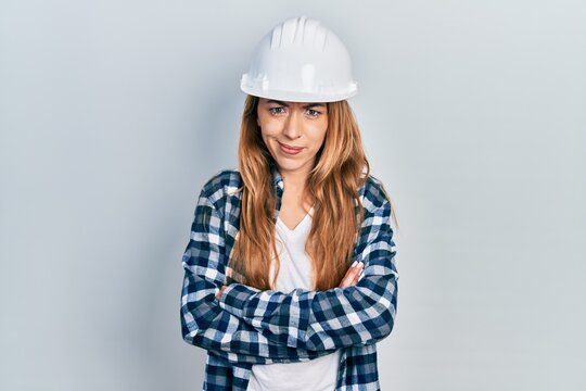 Young caucasian woman wearing architect hardhat skeptic and nervous, disapproving expression on face with crossed arms. negative person.