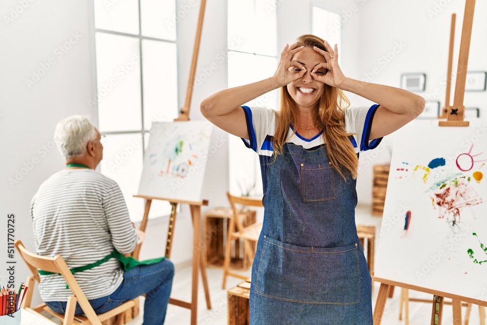 Canvas Prints Hispanic woman wearing apron at art studio doing ok gesture like binoculars sticking tongue out, eyes looking through fingers. crazy expression.