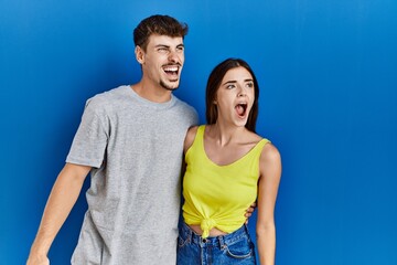 Fototapeta premium Young hispanic couple standing together over blue background angry and mad screaming frustrated and furious, shouting with anger. rage and aggressive concept.
