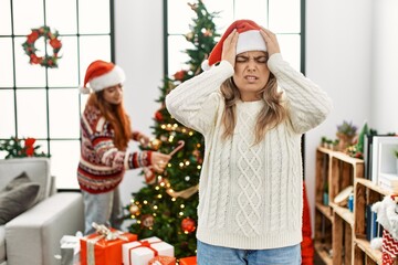 Beautiful couple at home standing by the christmas tree suffering from headache desperate and...