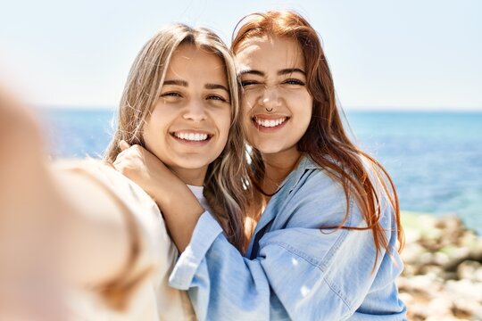 Young lesbian couple of two women in love at the beach. Beautiful women together at the beach in a romantic relationship taking selfie photo with smartphone