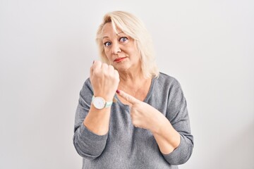 Middle age caucasian woman standing over white background in hurry pointing to watch time,...