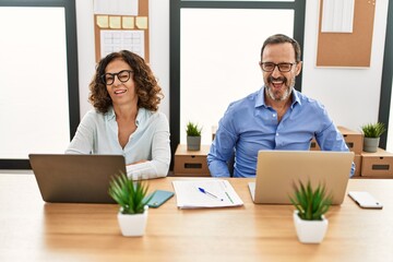 Middle age hispanic woman and man sitting with laptop at the office winking looking at the camera...