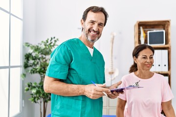 Fototapeta premium Middle age man and woman wearing physiotherapist uniform having rehab session at physiotherapy clinic