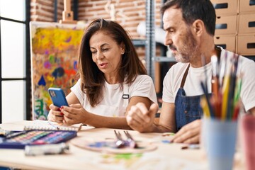 Fototapeta premium Middle age man and woman artists drawing on notebook using smartphone at art studio