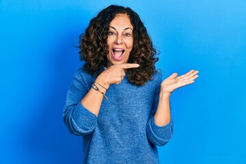 Middle age hispanic woman wearing casual clothes amazed and smiling to the camera while presenting with hand and pointing with finger.