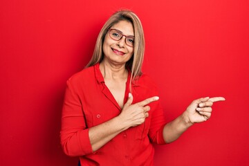 Naklejka premium Middle age hispanic woman wearing casual clothes and glasses smiling and looking at the camera pointing with two hands and fingers to the side.