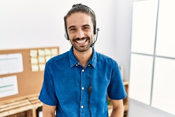 Young hispanic man with beard wearing call center agent headset at the office looking positive and...