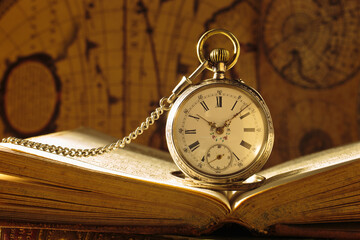 Antique pocket watch on opened old book. Old map on background