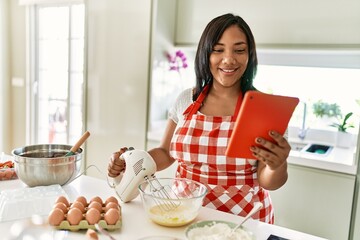 Hispanic brunette woman preparing cake looking at online recipe at the kitchen