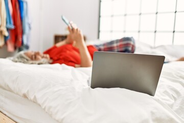 Middle age grey-haired woman using smartphone lying on the bed at bedroom.
