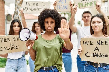 Group of young friends protesting and giving slogans at the street with open hand doing stop sign with serious and confident expression, defense gesture - obrazy, fototapety, plakaty