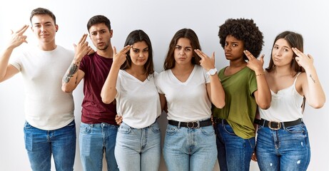 Group of young friends standing together over isolated background shooting and killing oneself pointing hand and fingers to head like gun, suicide gesture.