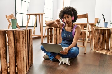 Young african american woman with afro hair at art studio using laptop with angry face, negative...