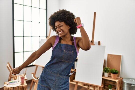 Young african american woman with afro hair at art studio dancing happy and cheerful, smiling moving casual and confident listening to music