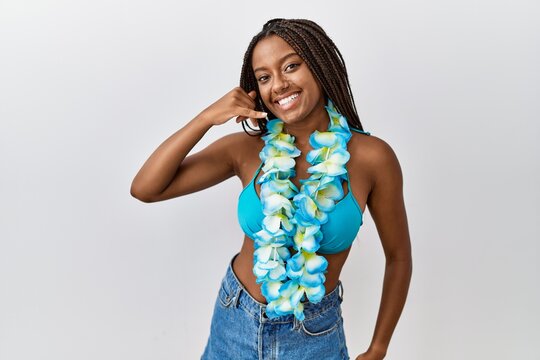 Young african american woman with braids wearing bikini and hawaiian lei smiling doing phone gesture with hand and fingers like talking on the telephone. communicating concepts.