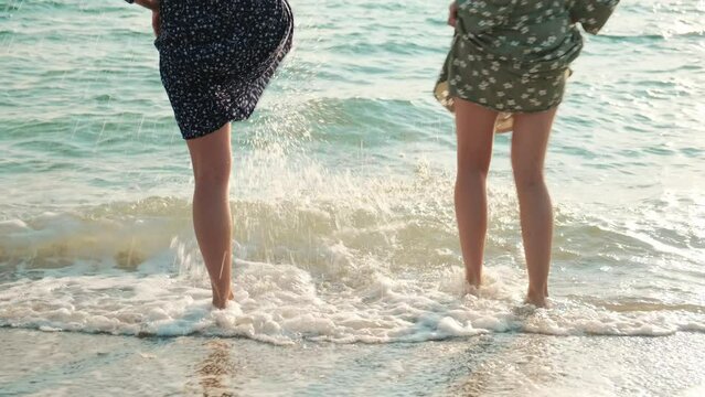 Women legs in the sea water. Carefree girls barefoot playing together enjoying summer at the beach, jumping at seaside.