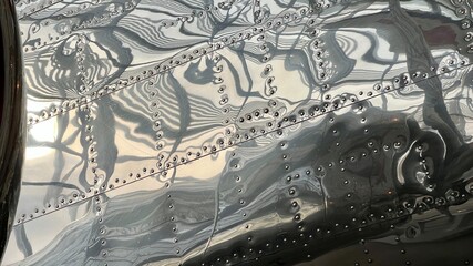 Detail of aircraft covered in polished metal panels, riveted in place with abstract reflections. Suitable for background for graphics and text