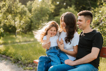 Fototapeta premium Young cheerful family with daughter having fun outdoors