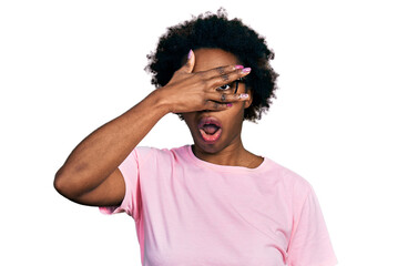 African american woman with afro hair wearing casual clothes and glasses peeking in shock covering face and eyes with hand, looking through fingers with embarrassed expression.