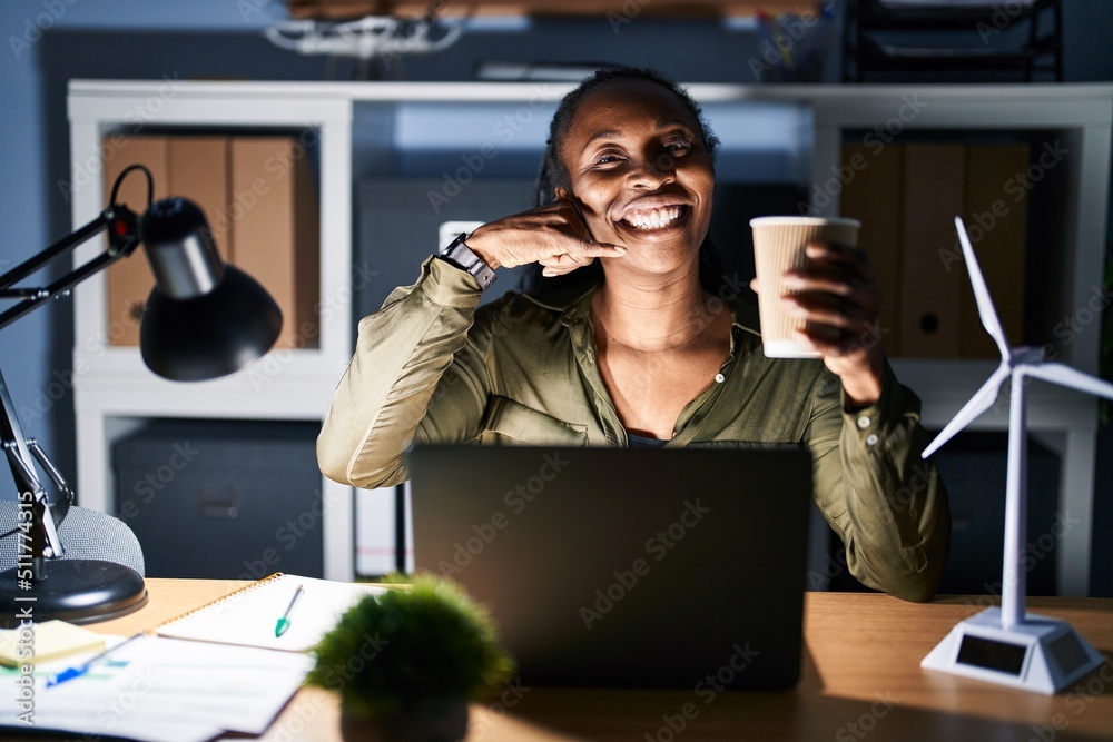 Canvas Prints African woman working using computer laptop at night smiling doing phone gesture with hand and fingers like talking on the telephone. communicating concepts.