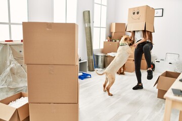 Young hispanic woman wearing funny cardboard on head playing with dogs at new home